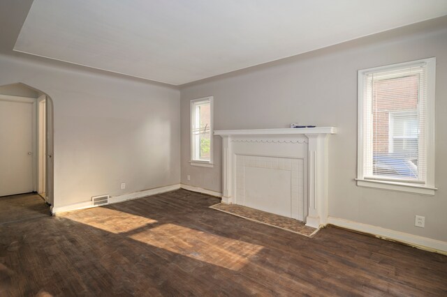 unfurnished living room featuring a tile fireplace and dark wood-type flooring