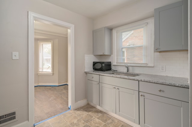 kitchen with decorative backsplash, gray cabinets, light stone countertops, and sink