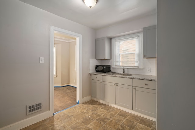 kitchen with backsplash, light stone counters, and sink