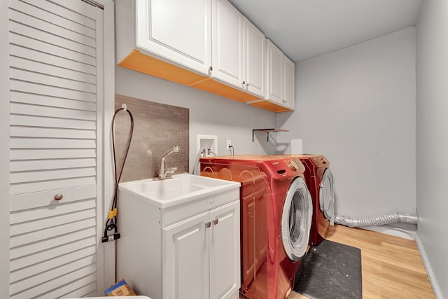 laundry room featuring cabinets, light wood-type flooring, sink, and separate washer and dryer