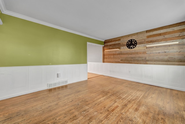 empty room with hardwood / wood-style floors, ornamental molding, and wooden walls