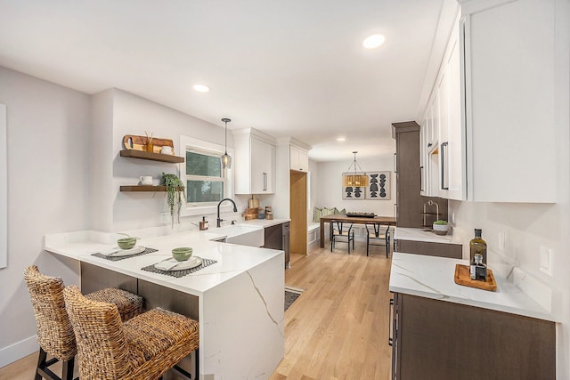 kitchen featuring a breakfast bar, light wood-style flooring, decorative light fixtures, white cabinetry, and a peninsula