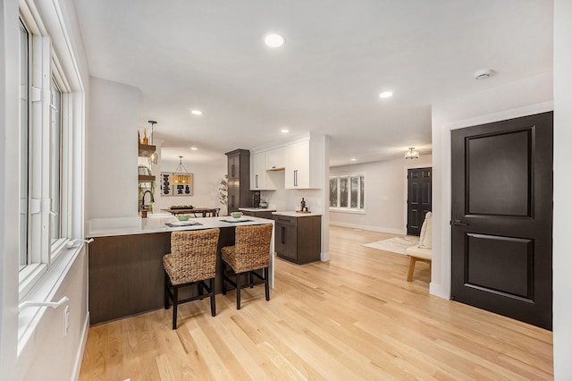 kitchen featuring a kitchen bar, a peninsula, light countertops, and light wood-type flooring