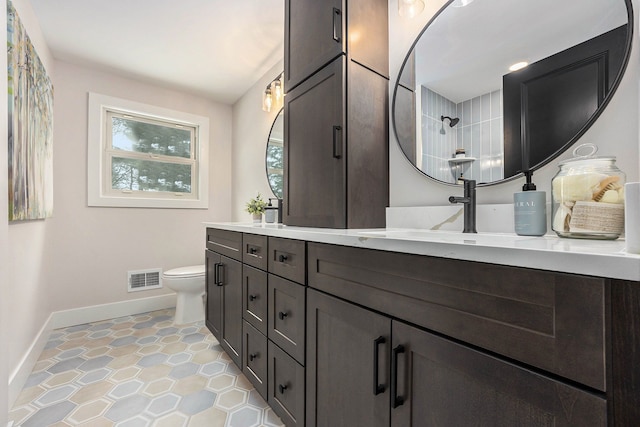 bathroom featuring visible vents, double vanity, toilet, baseboards, and a sink
