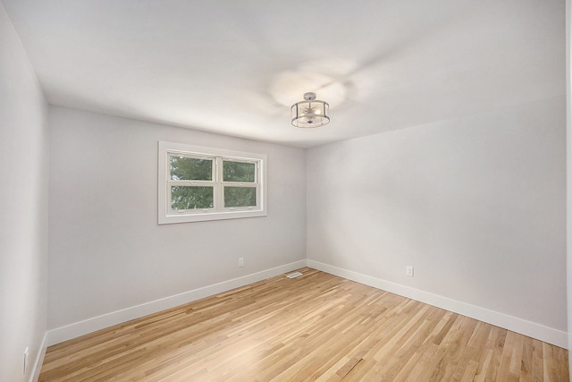 empty room with baseboards, light wood-type flooring, a chandelier, and visible vents