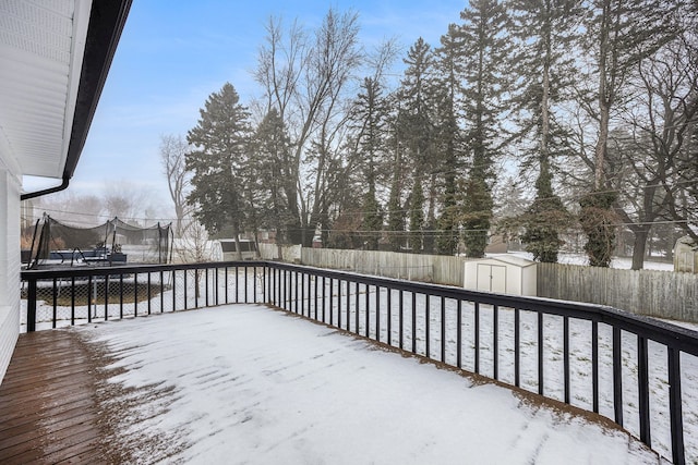 snow covered deck featuring a fenced backyard, a trampoline, an outdoor structure, and a shed