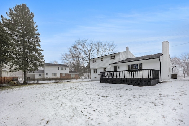 snow covered rear of property featuring a deck, fence, and a chimney