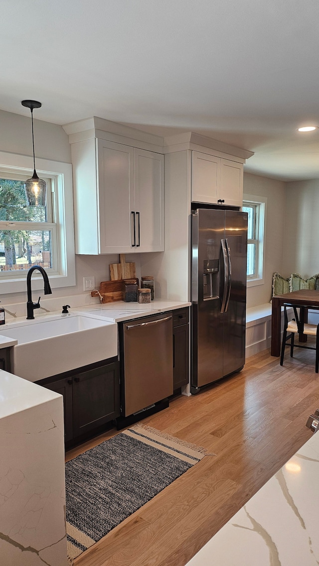 kitchen featuring light stone countertops, pendant lighting, light wood-type flooring, stainless steel appliances, and a sink