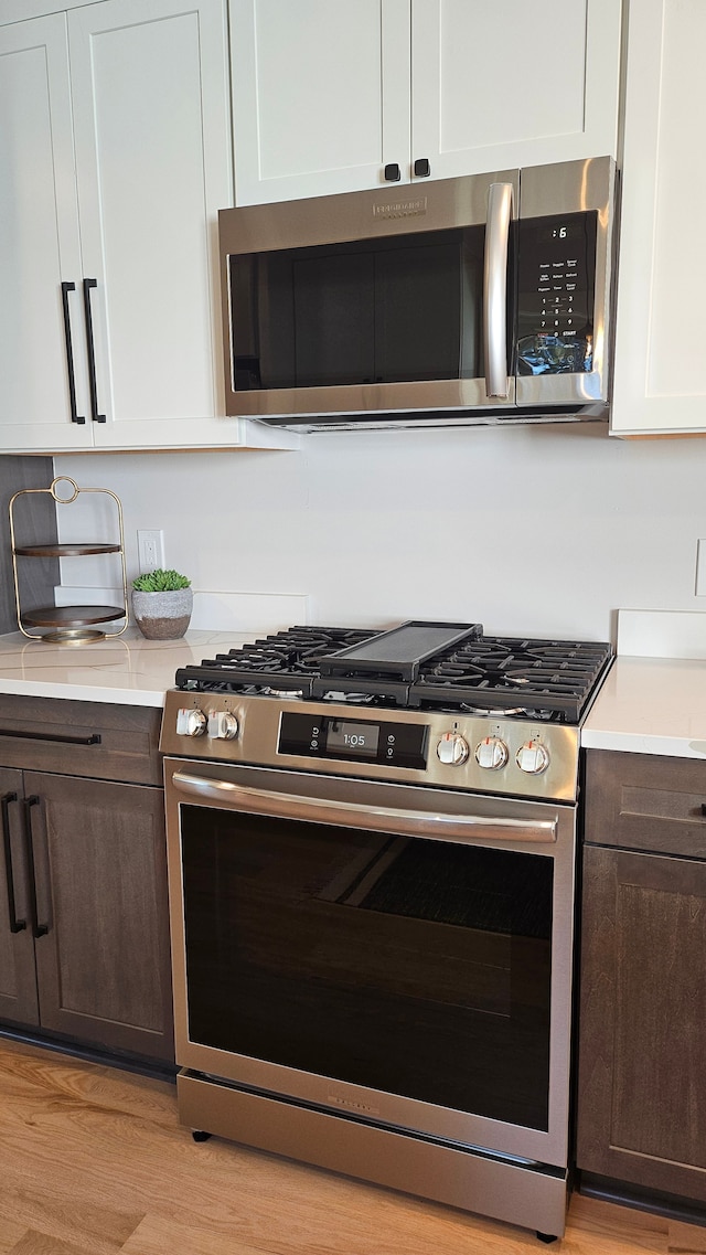 kitchen featuring white cabinetry, dark brown cabinetry, appliances with stainless steel finishes, and light countertops