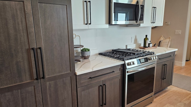 kitchen with light wood-style floors, appliances with stainless steel finishes, light stone counters, and dark brown cabinetry
