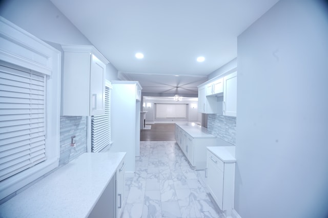 kitchen with backsplash, white cabinetry, and light stone countertops