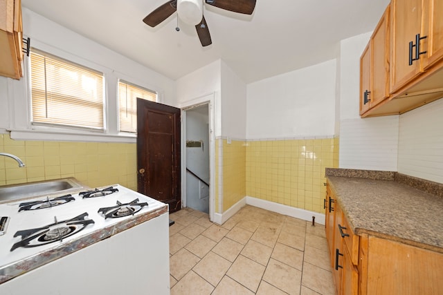 kitchen featuring white gas range, ceiling fan, tile walls, and sink