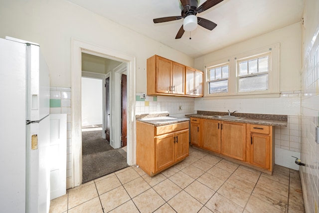 kitchen featuring ceiling fan, white fridge with ice dispenser, sink, light tile patterned flooring, and tile walls