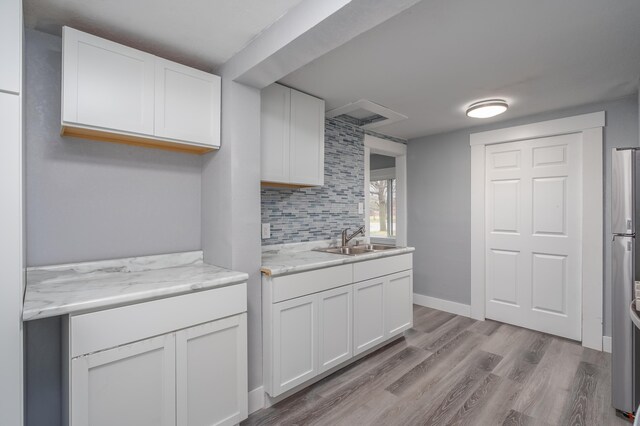 kitchen featuring white cabinetry, sink, light stone countertops, light hardwood / wood-style flooring, and decorative backsplash