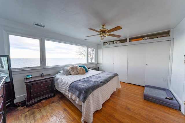 bedroom with a water view, ceiling fan, and wood-type flooring