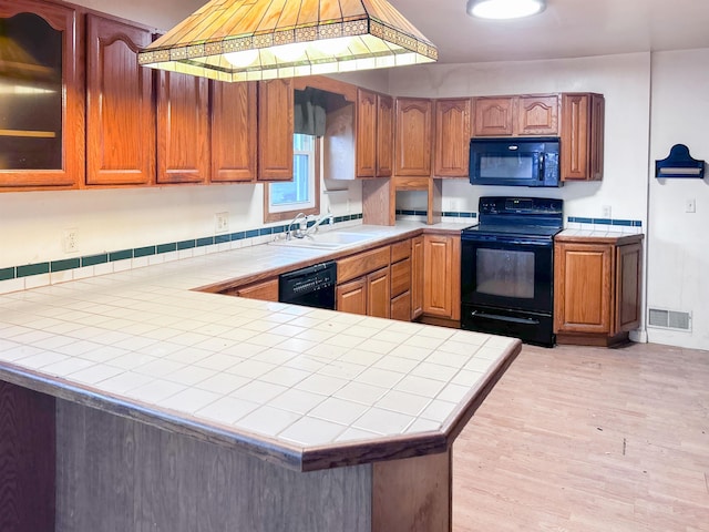 kitchen with tile countertops, black appliances, sink, light hardwood / wood-style flooring, and kitchen peninsula