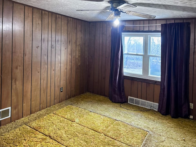 empty room featuring wooden walls, ceiling fan, and a textured ceiling