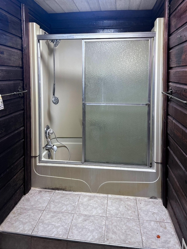 bathroom with wood walls and combined bath / shower with glass door