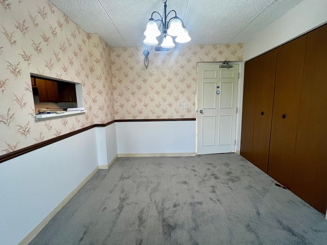 empty room with a notable chandelier, light colored carpet, and a textured ceiling