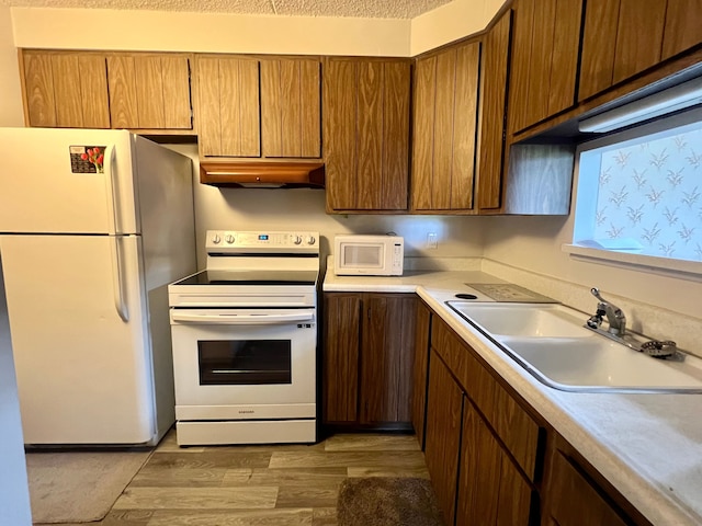 kitchen with a textured ceiling, white appliances, light hardwood / wood-style flooring, and sink