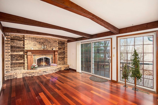 unfurnished living room with beamed ceiling, plenty of natural light, hardwood / wood-style floors, and a brick fireplace