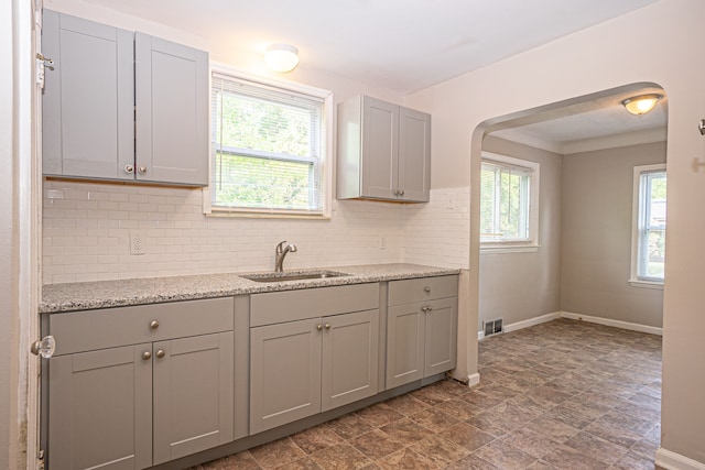 kitchen featuring light stone countertops, gray cabinets, tasteful backsplash, and sink