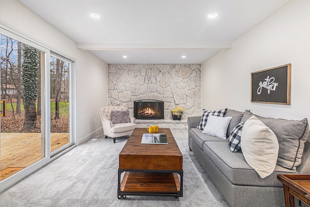 carpeted living room with a stone fireplace and beamed ceiling