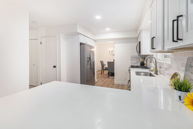 kitchen featuring sink, light wood-type flooring, tasteful backsplash, white cabinetry, and stainless steel appliances