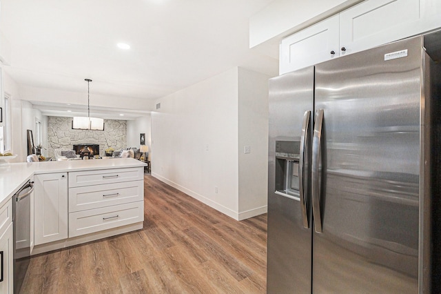 kitchen featuring white cabinetry, stainless steel appliances, pendant lighting, light hardwood / wood-style floors, and a fireplace