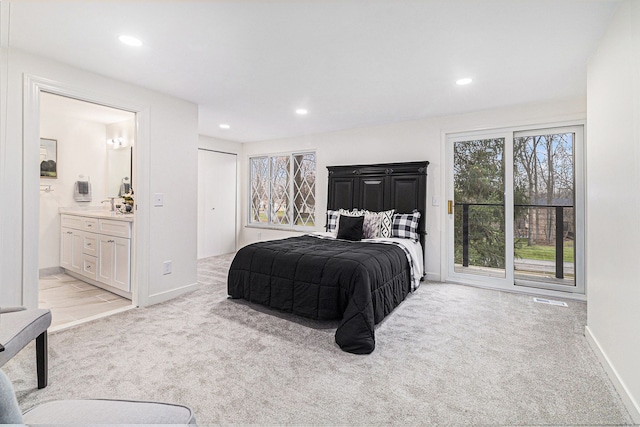 bedroom with a closet, light colored carpet, and ensuite bath