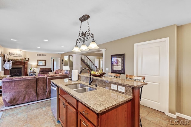 kitchen featuring ornate columns, sink, dishwasher, hanging light fixtures, and a kitchen island with sink