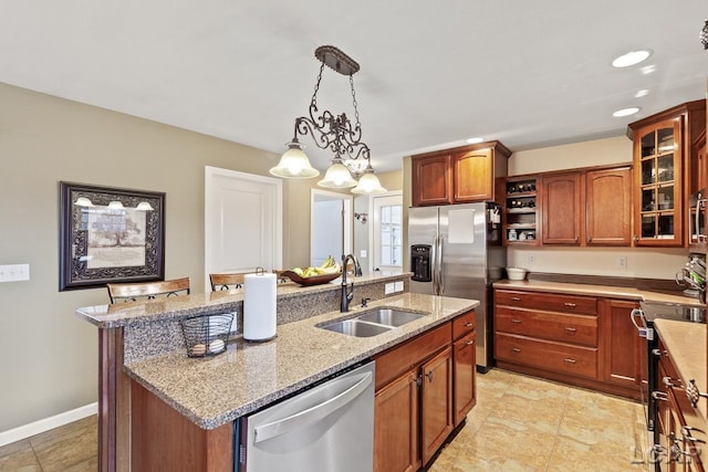 kitchen featuring light stone countertops, sink, hanging light fixtures, stainless steel appliances, and a center island with sink