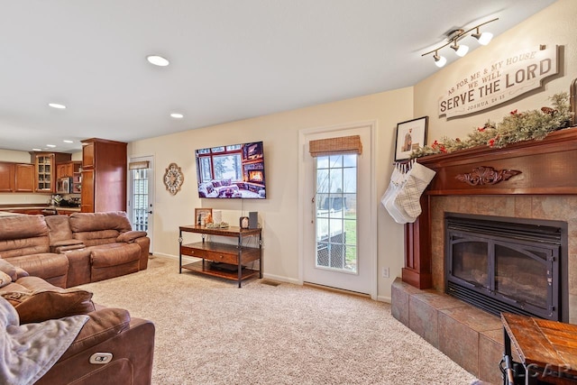 living room with a tile fireplace, light carpet, and rail lighting