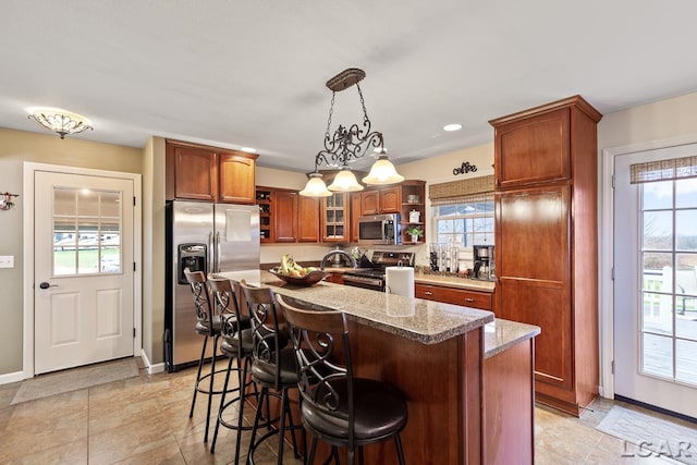 kitchen with light stone countertops, appliances with stainless steel finishes, decorative light fixtures, and a kitchen island