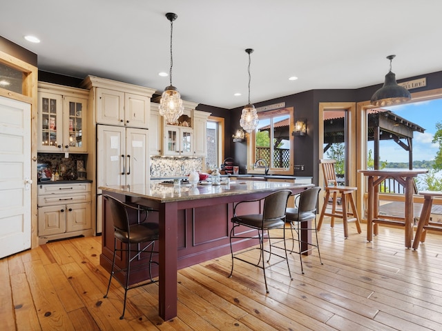 kitchen featuring cream cabinetry, stone countertops, pendant lighting, and decorative backsplash