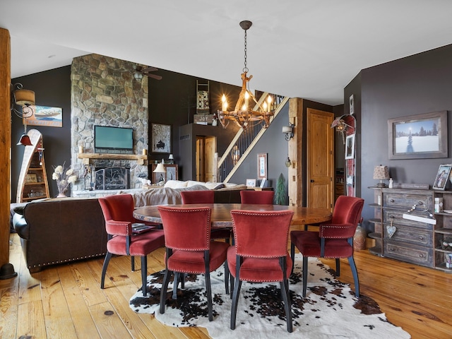 dining space with hardwood / wood-style flooring, a notable chandelier, a stone fireplace, and vaulted ceiling