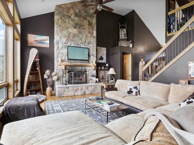 living room with wood-type flooring, high vaulted ceiling, a stone fireplace, and ceiling fan