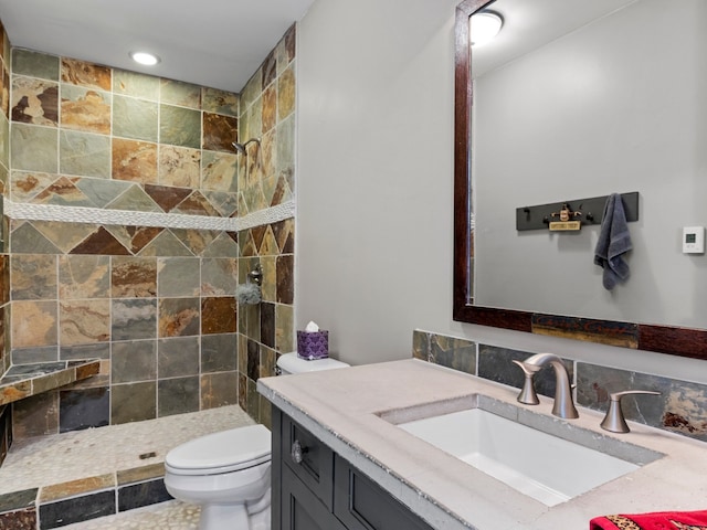 bathroom featuring a tile shower, vanity, and toilet