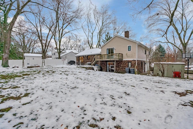 snow covered rear of property with a jacuzzi and a deck