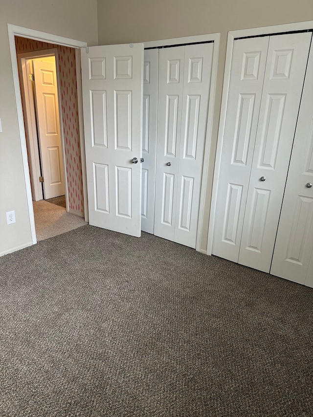 unfurnished bedroom featuring multiple closets and dark colored carpet