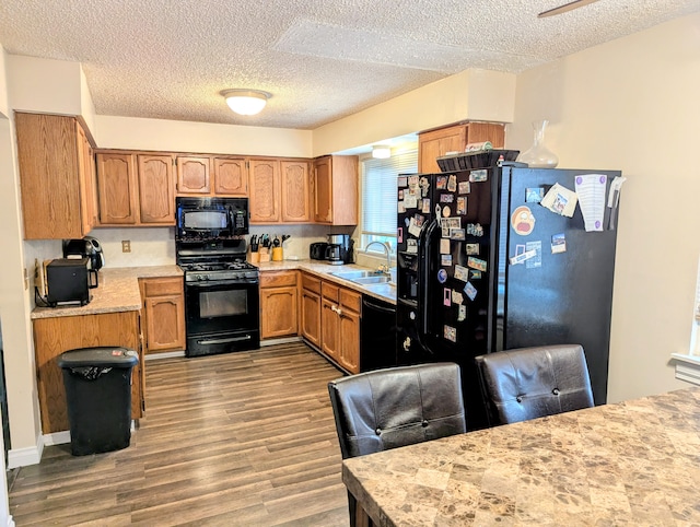 kitchen with a textured ceiling, sink, hardwood / wood-style flooring, and black appliances