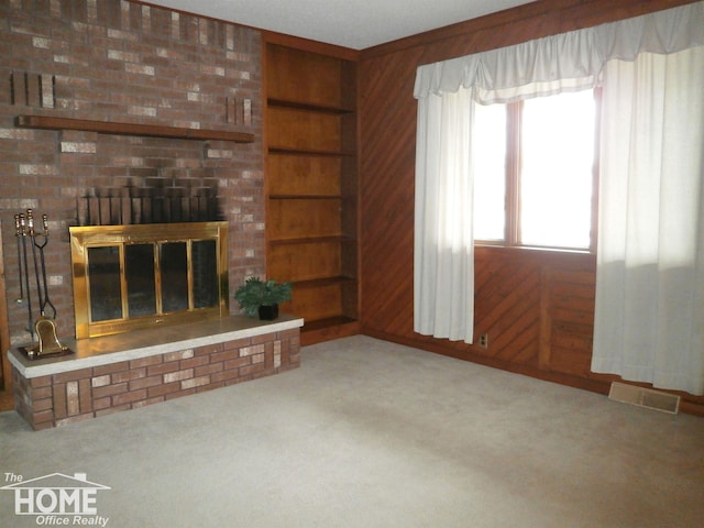 unfurnished living room with carpet flooring, wood walls, a fireplace, and built in features