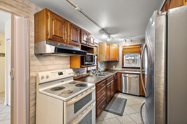 kitchen with wooden walls, sink, light tile patterned flooring, and appliances with stainless steel finishes