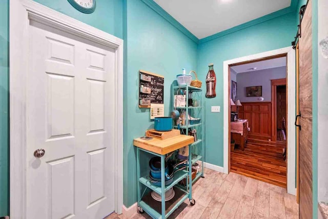 corridor featuring light wood-type flooring, a barn door, and ornamental molding