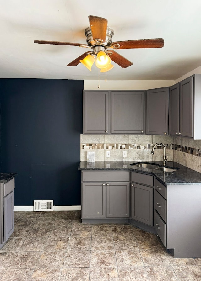 kitchen featuring gray cabinetry, ceiling fan, sink, dark stone countertops, and decorative backsplash