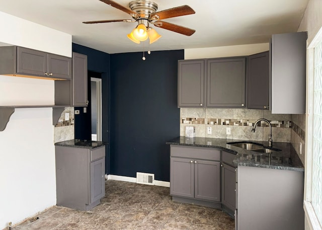 kitchen featuring ceiling fan, sink, backsplash, dark stone countertops, and gray cabinets