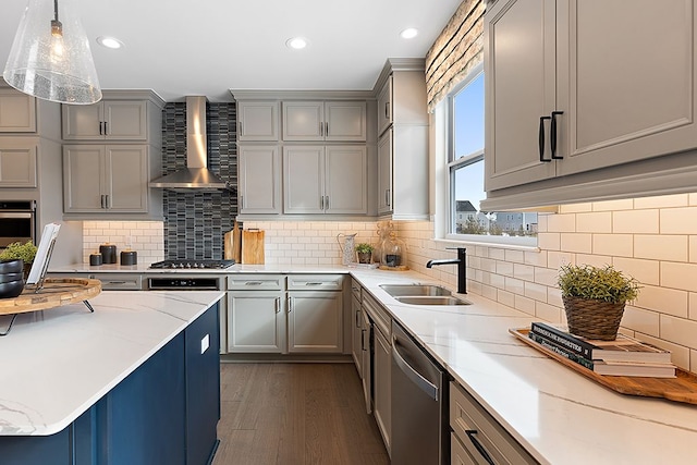 kitchen featuring appliances with stainless steel finishes, backsplash, wall chimney exhaust hood, sink, and hanging light fixtures