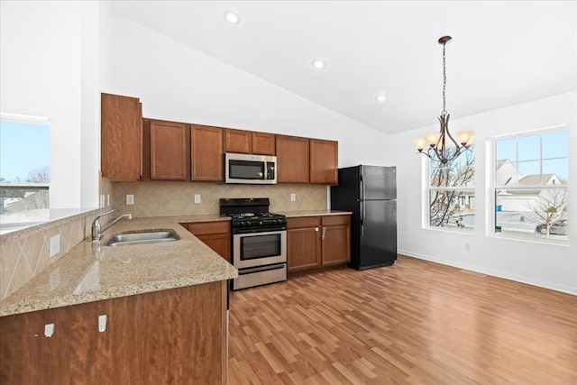 kitchen featuring sink, an inviting chandelier, light stone counters, appliances with stainless steel finishes, and light wood-type flooring