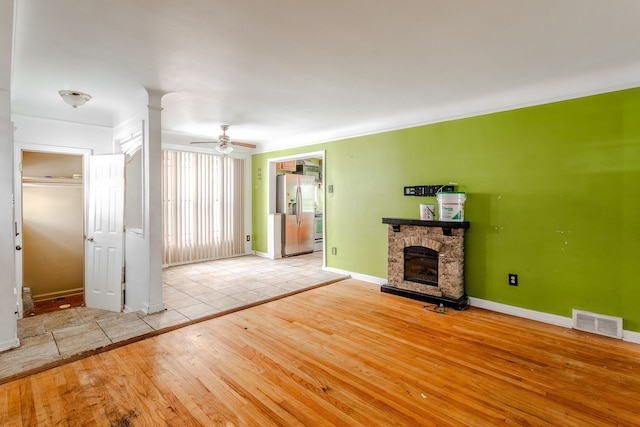 unfurnished living room with a stone fireplace, ceiling fan, light hardwood / wood-style flooring, and crown molding