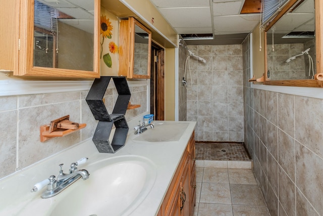 bathroom featuring a tile shower, tile patterned floors, a paneled ceiling, vanity, and tile walls